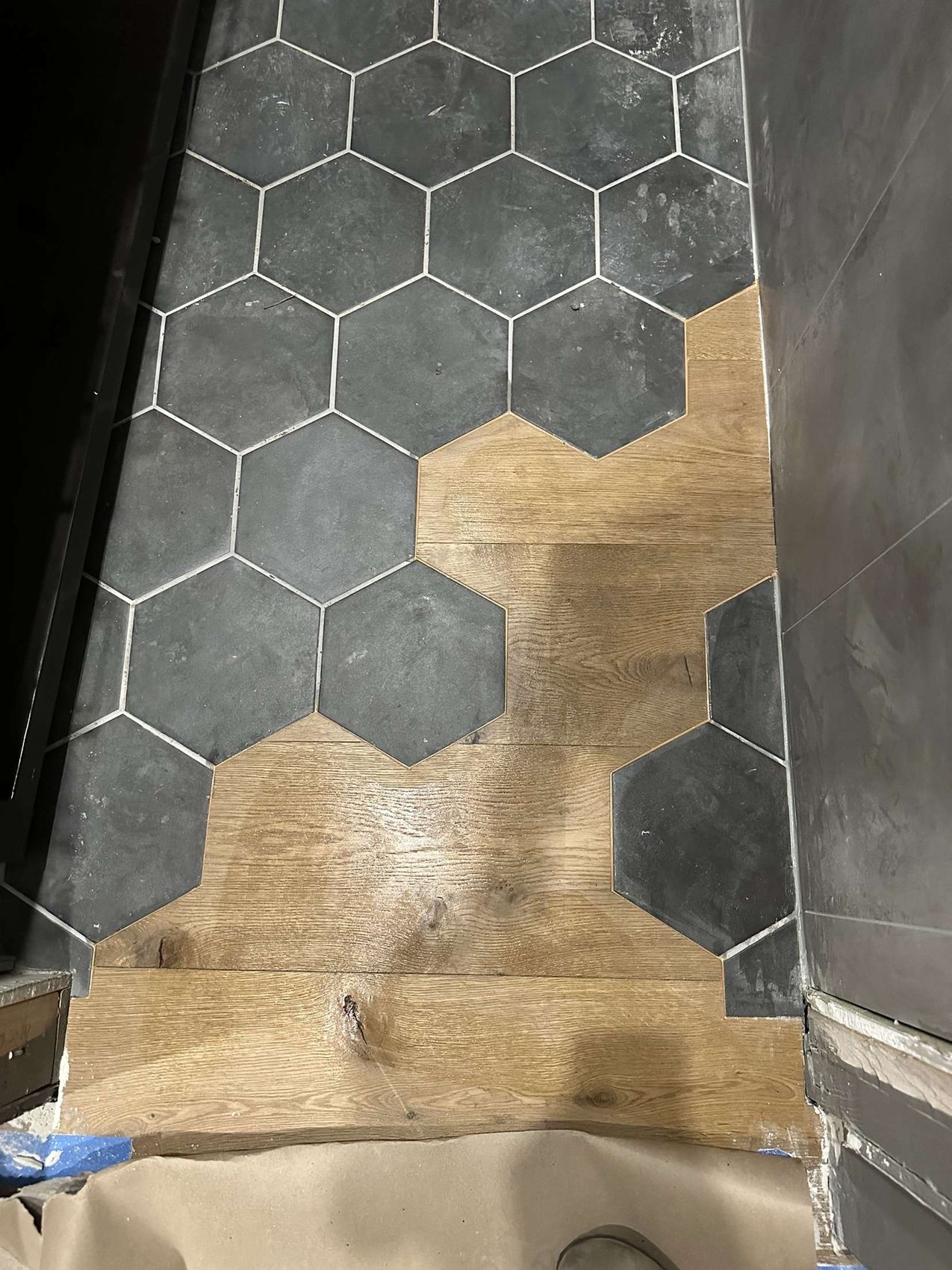Wood-look plank flooring hand-scribed around black hexagon porcelain tile at a doorway